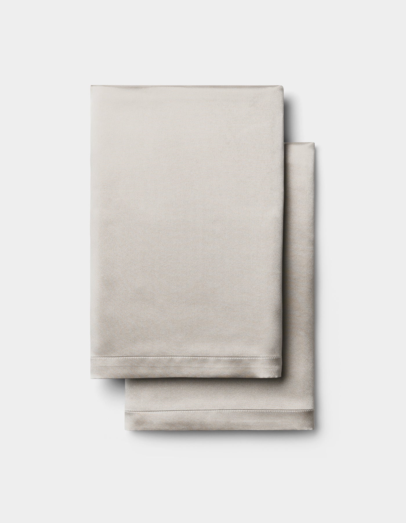 Two neatly folded Cozy Earth Silk Pillowcases in light beige are stacked together against a plain white background.|Color:Dove Grey