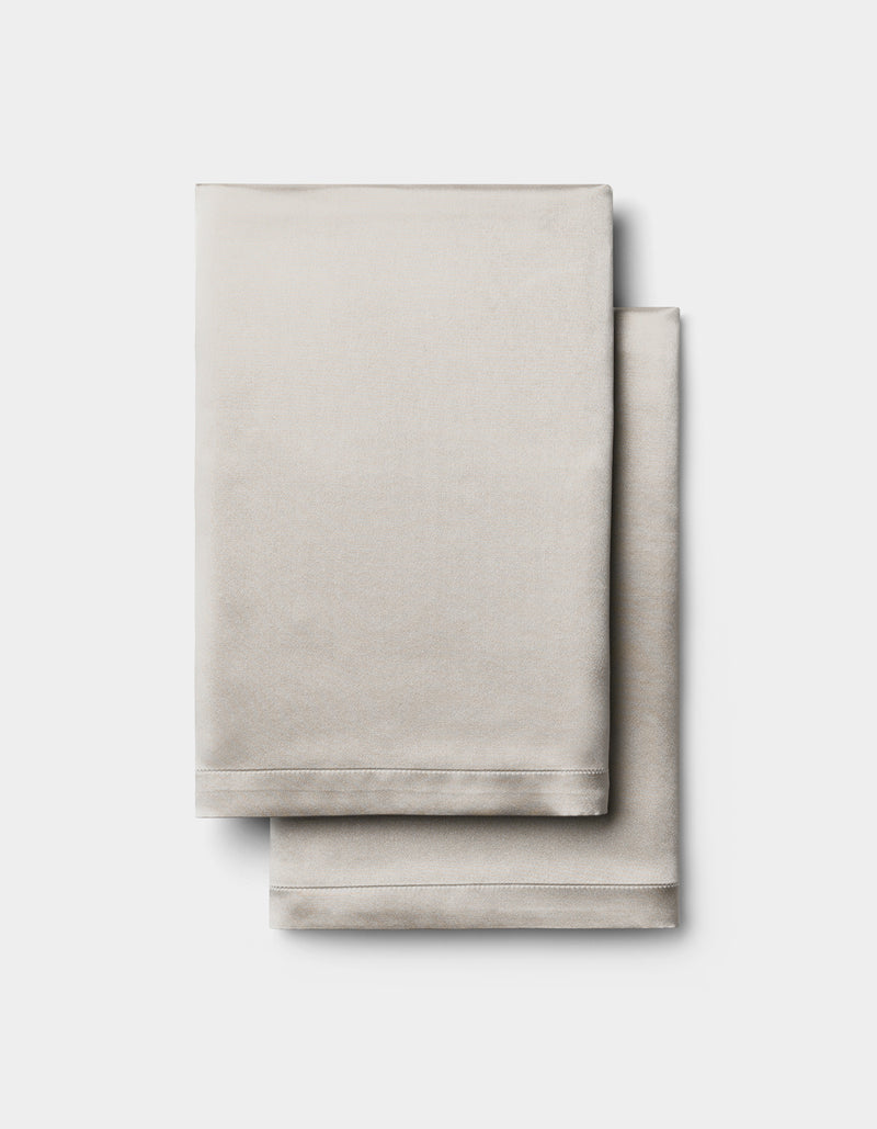 Two neatly folded Cozy Earth Silk Pillowcases in light beige are stacked together against a plain white background.
