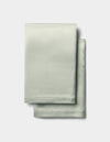 Two neatly folded Cozy Earth Silk Pillowcases in light sage green, featuring a smooth, satin-like texture, are stacked on a plain white background.|Color:Laurel