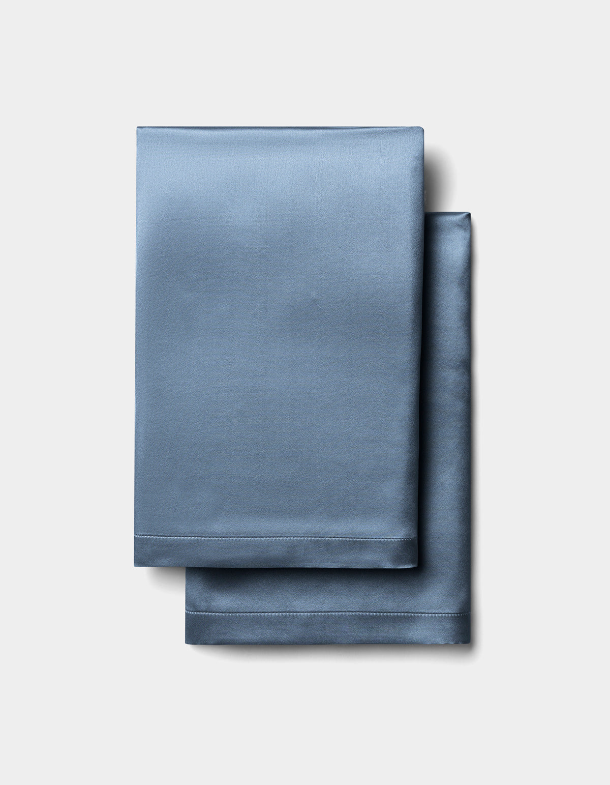 Cozy Earth Silk Pillowcases in light blue are folded and stacked neatly on a light grey background.