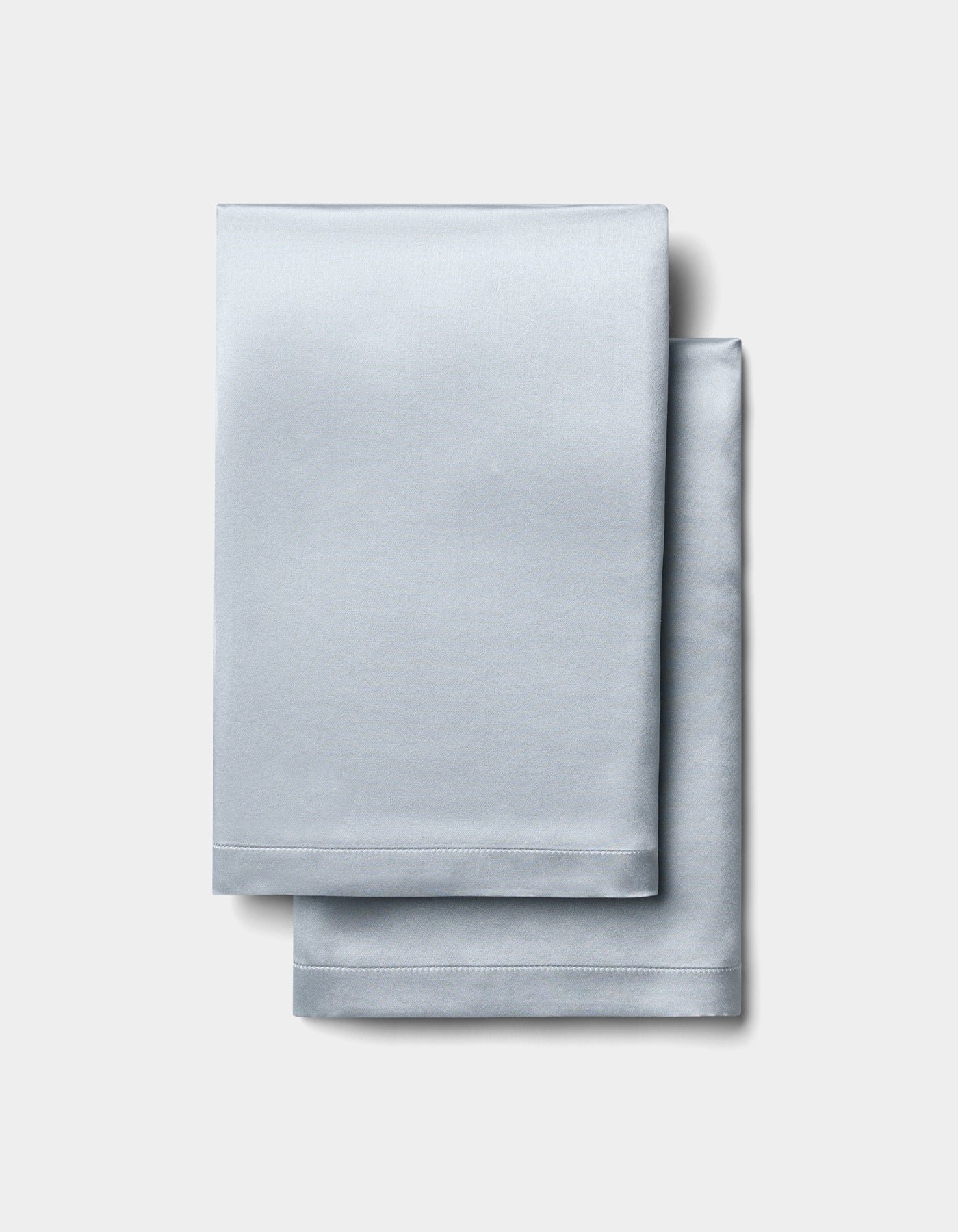 Two neatly folded Cozy Earth Silk Pillowcases are stacked on a plain, light gray background. 