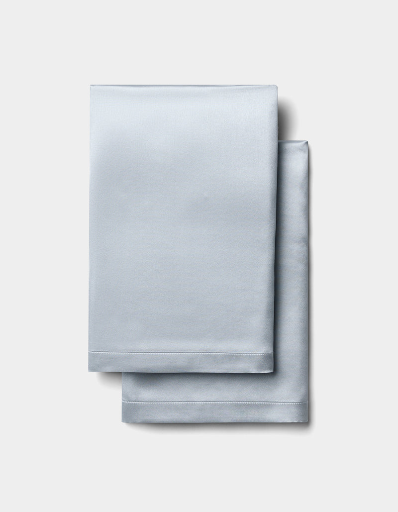 Two neatly folded Cozy Earth Silk Pillowcases are stacked on a plain, light gray background.