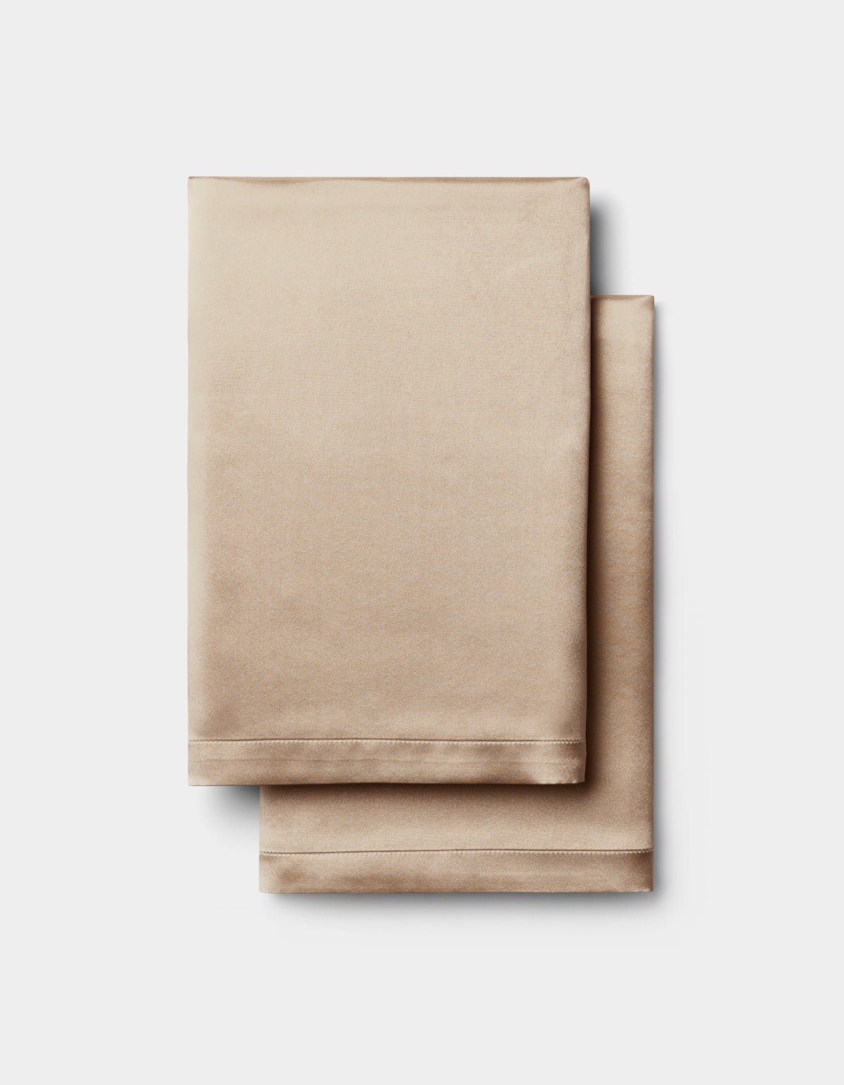 Two neatly folded Cozy Earth Silk Pillowcases in a champagne hue are stacked on a plain white background.