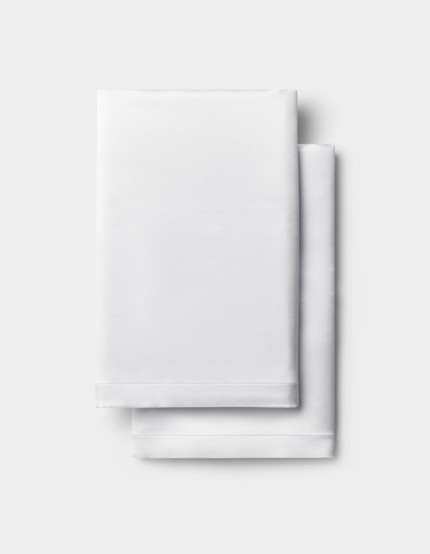 A neatly folded white Silk Pillowcase by Cozy Earth is stacked on a light gray background.