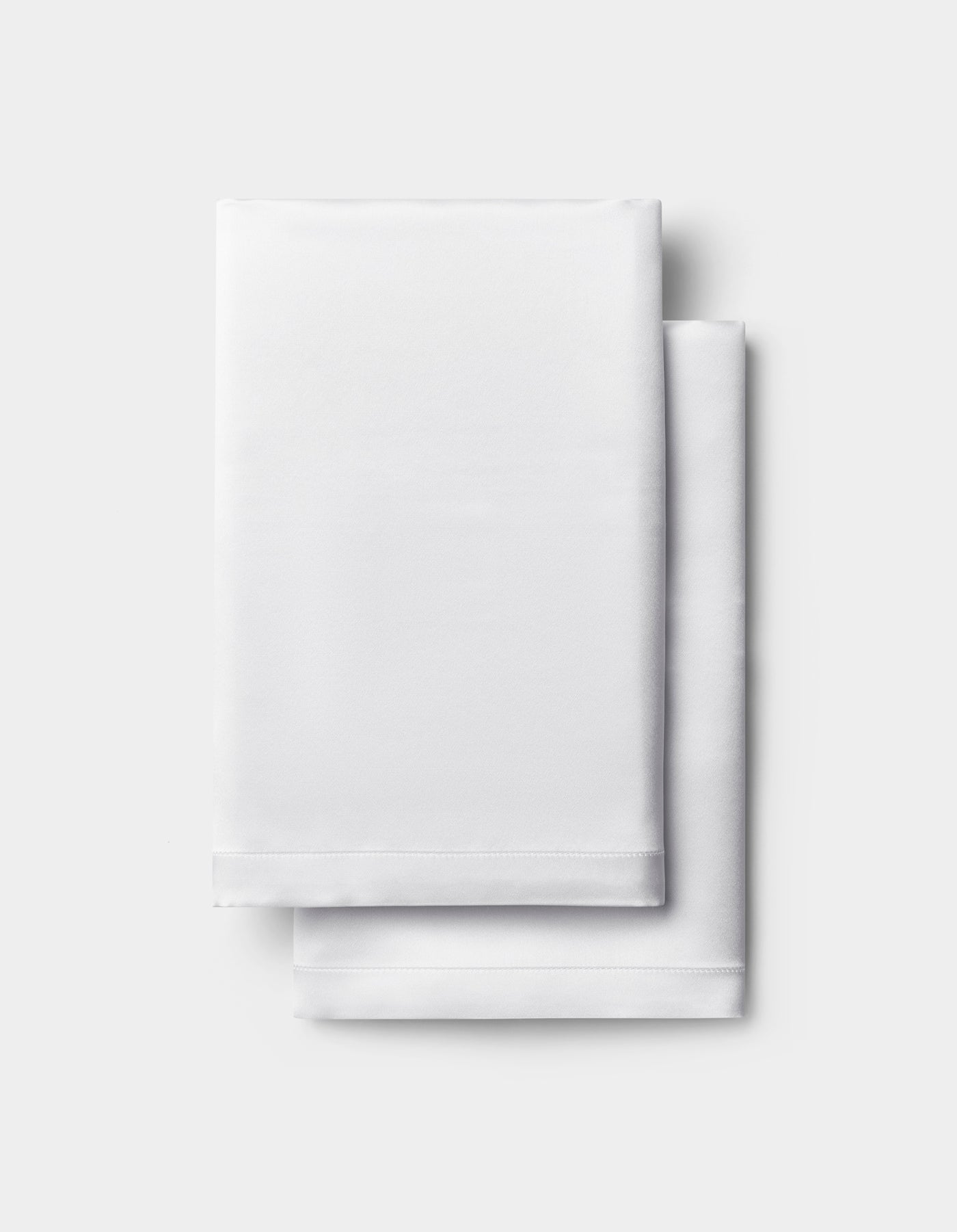 A neatly folded white Silk Pillowcase by Cozy Earth is stacked on a light gray background.