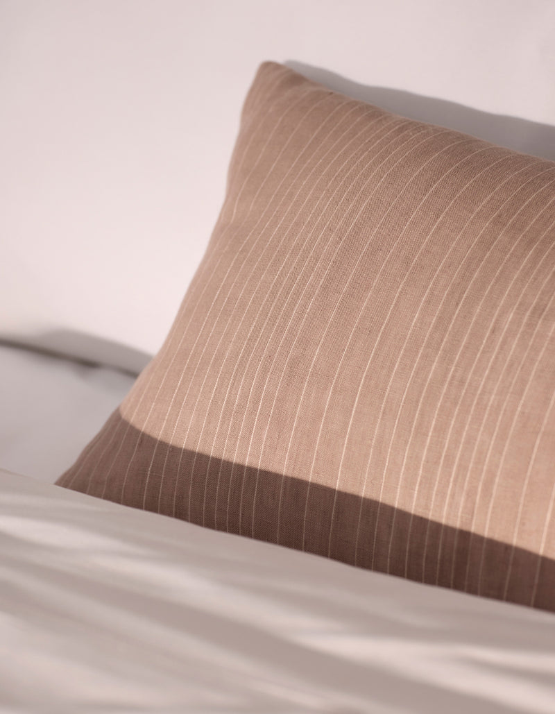 The Cozy Earth Striped Throw Pillow, in beige with subtle vertical stripes, rests against white bedding in soft natural light.