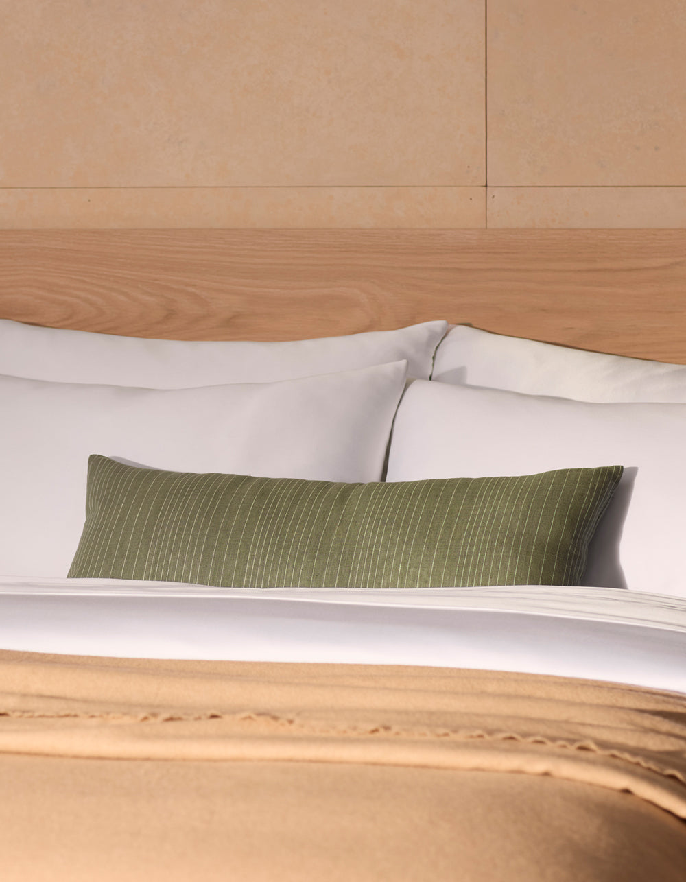A neatly made bed with white linens and pillows, a Cozy Earth Striped Throw Pillow as an accent, and a beige blanket at the foot, set against a light wood headboard and tan wall.