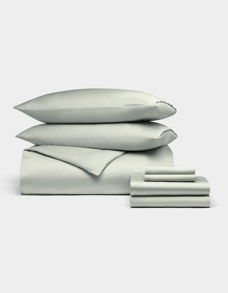 A neatly stacked Cozy Earth Bamboo Bedding Ultimate Bundle, featuring two pillows, a folded duvet, and folded sheets in pale green, displayed against a plain white background.