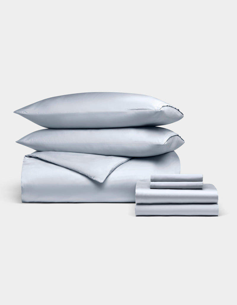 The Cozy Earth Bamboo Bedding Ultimate Bundle is showcased neatly with two stacked pillows, a duvet cover, a folded sheet, and two pillowcases in light gray, all set against a plain white background.