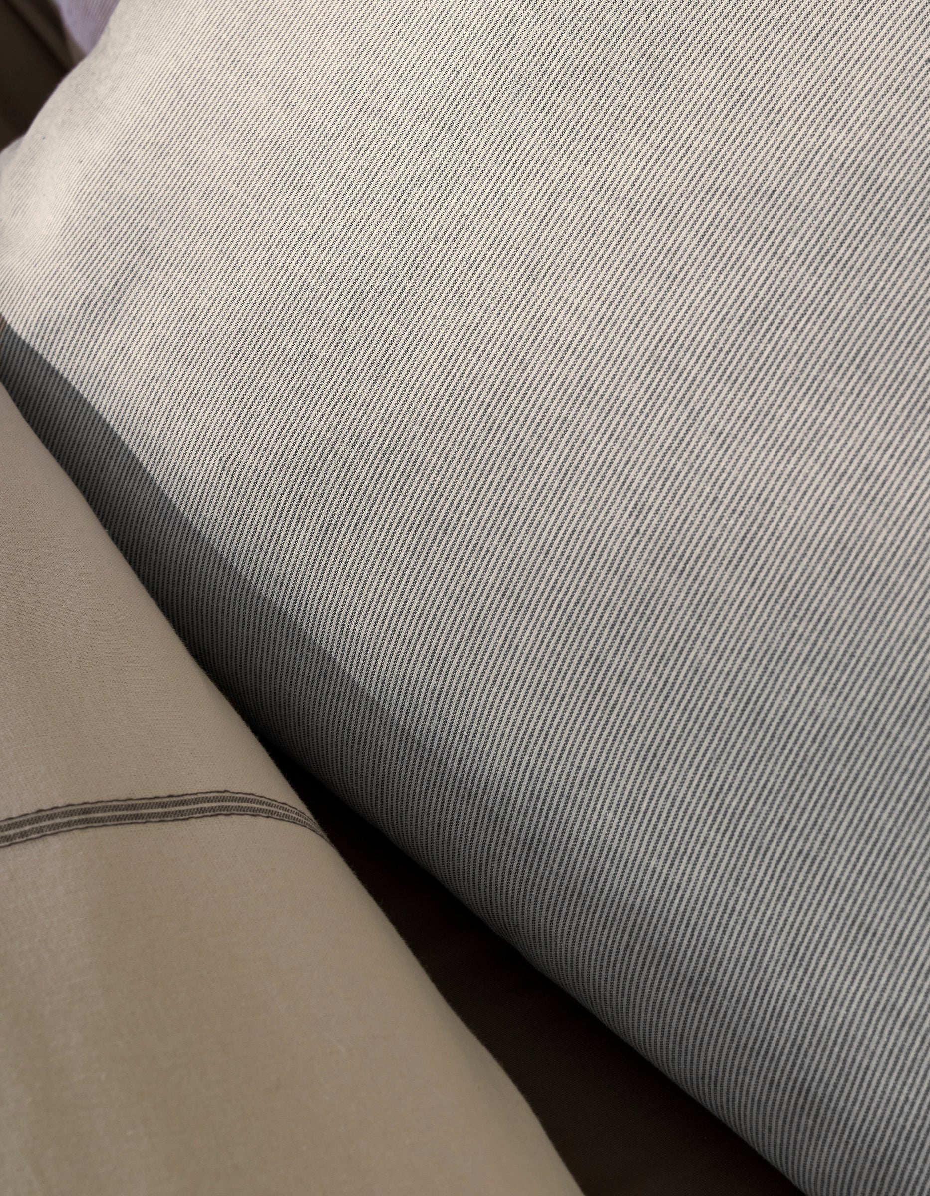 Close-up of Cozy Earth's Baja Double Sided Sham: one side features fine gray and white pinstripes, while the other is solid light beige with a simple dark line accent.|Color:Coal Stripe/Striped Alabaster