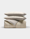 The Baja Duvet Bundle by Cozy Earth features a neatly folded beige comforter with thin light gray stripes, stacked with two matching pillows on top, all set against a plain white background.|Color:Coal Stripe/Striped Alabaster
