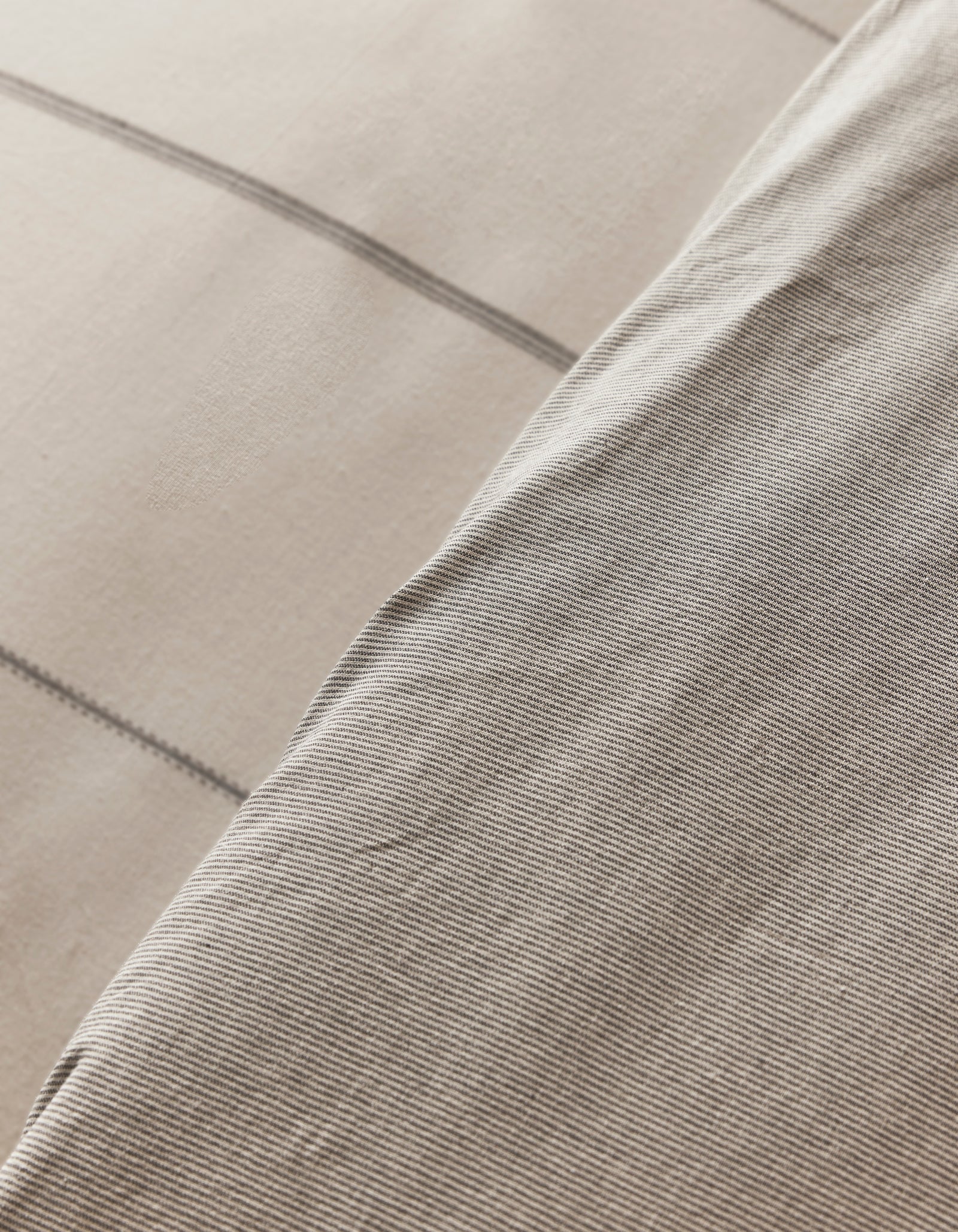 A close-up of the Cozy Earth Baja Duvet Cover shows two overlapping fabrics—one with thin light gray pinstripes, the other with a beige background and wide gray plaid lines. Both textiles feature a soft, woven texture.