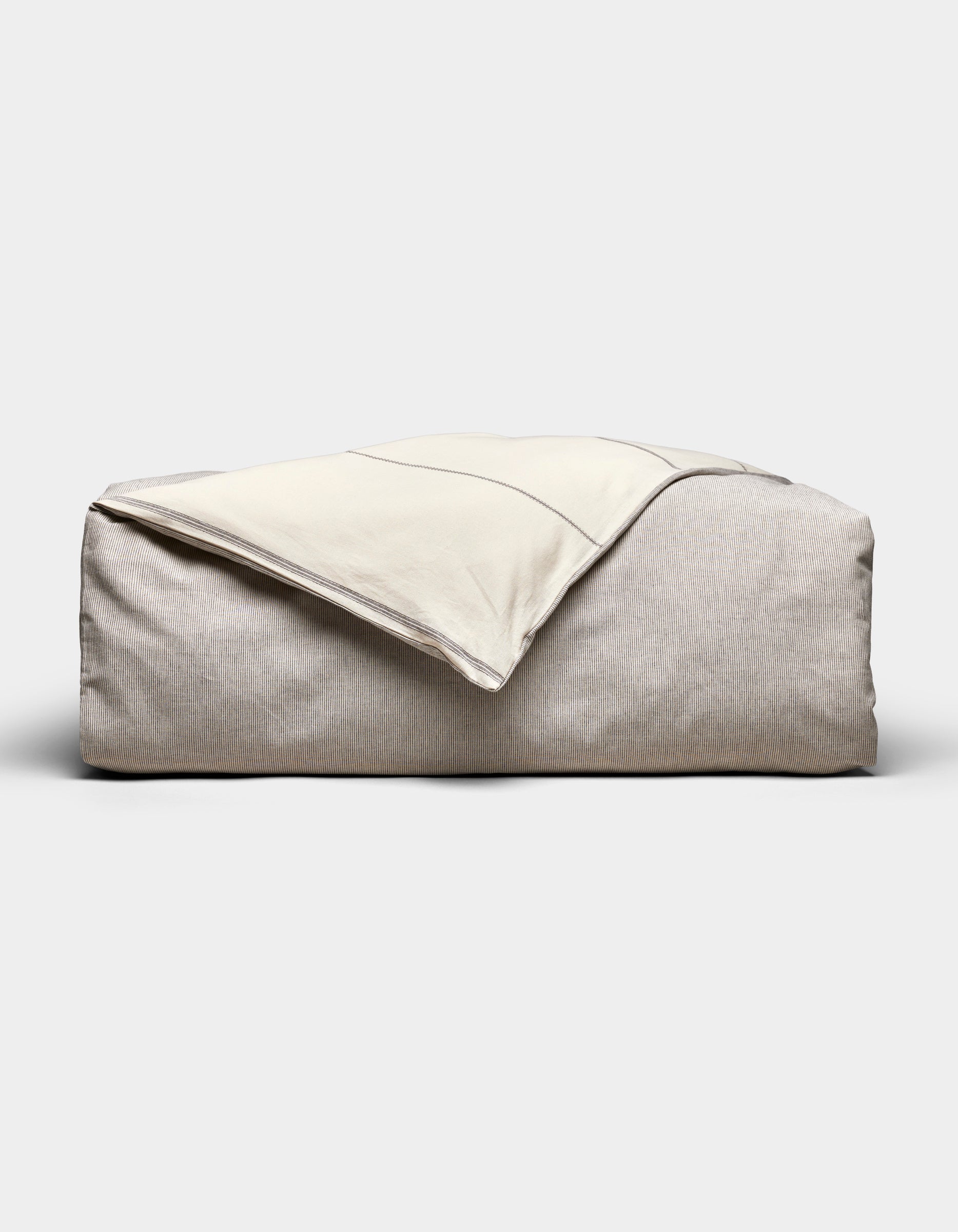The Baja Duvet Cover by Cozy Earth, in light beige, is shown with a cream-colored blanket draped diagonally over it against a plain, light background.|Color:Coal Stripe/Striped Alabaster