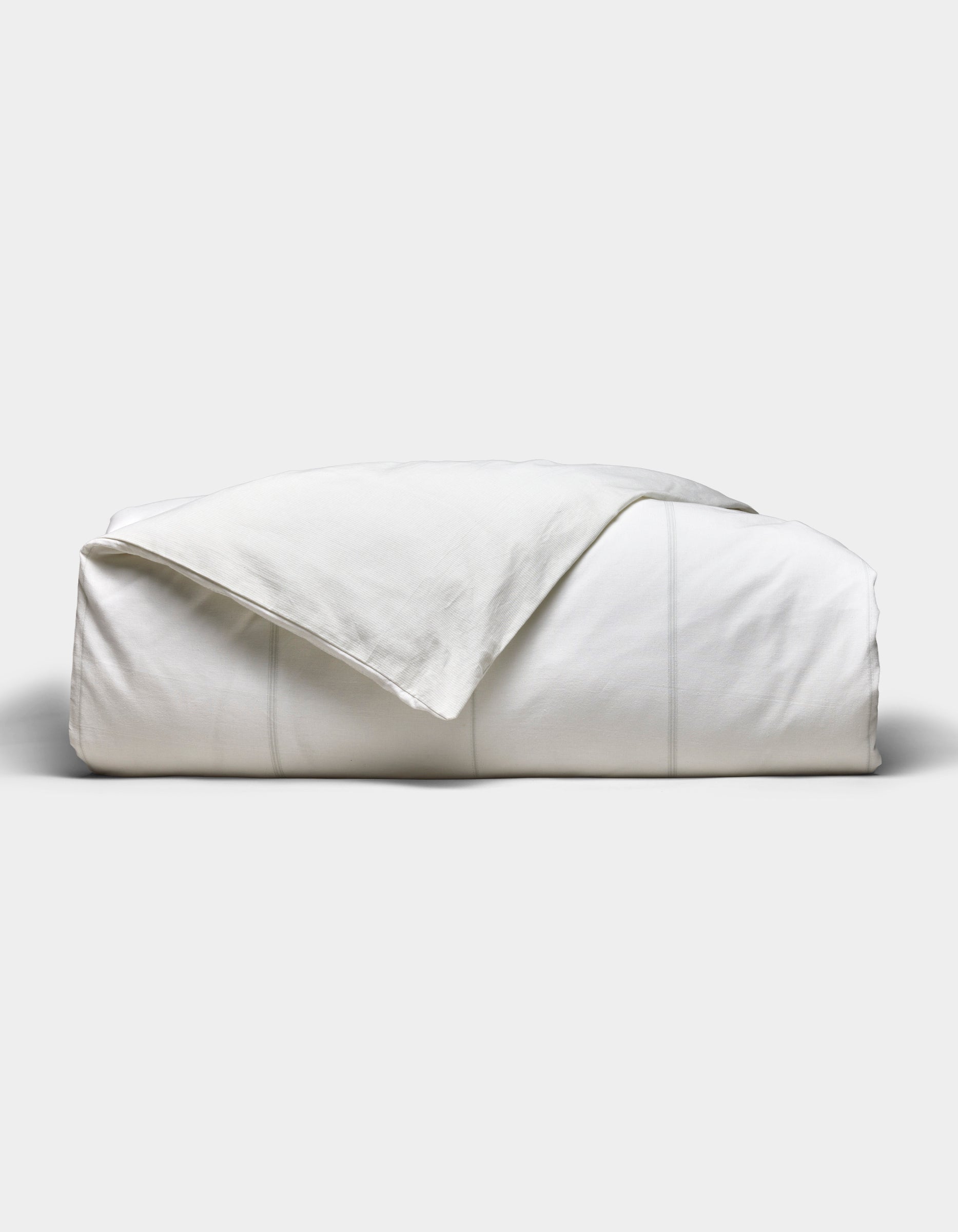 The Baja Duvet Cover by Cozy Earth is neatly folded with a slightly rumpled corner, set against a plain light gray background.|Color:Laurel Stripe/Striped Bone