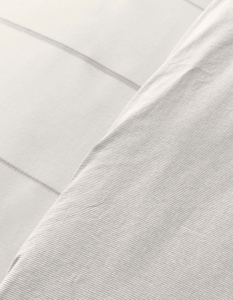 Close-up of Cozy Earth’s Baja Duvet Cover: overlapping white fabrics, one with subtle horizontal stripes and a smooth feel, the other featuring a faint grid pattern. Both offer a soft, clean look.