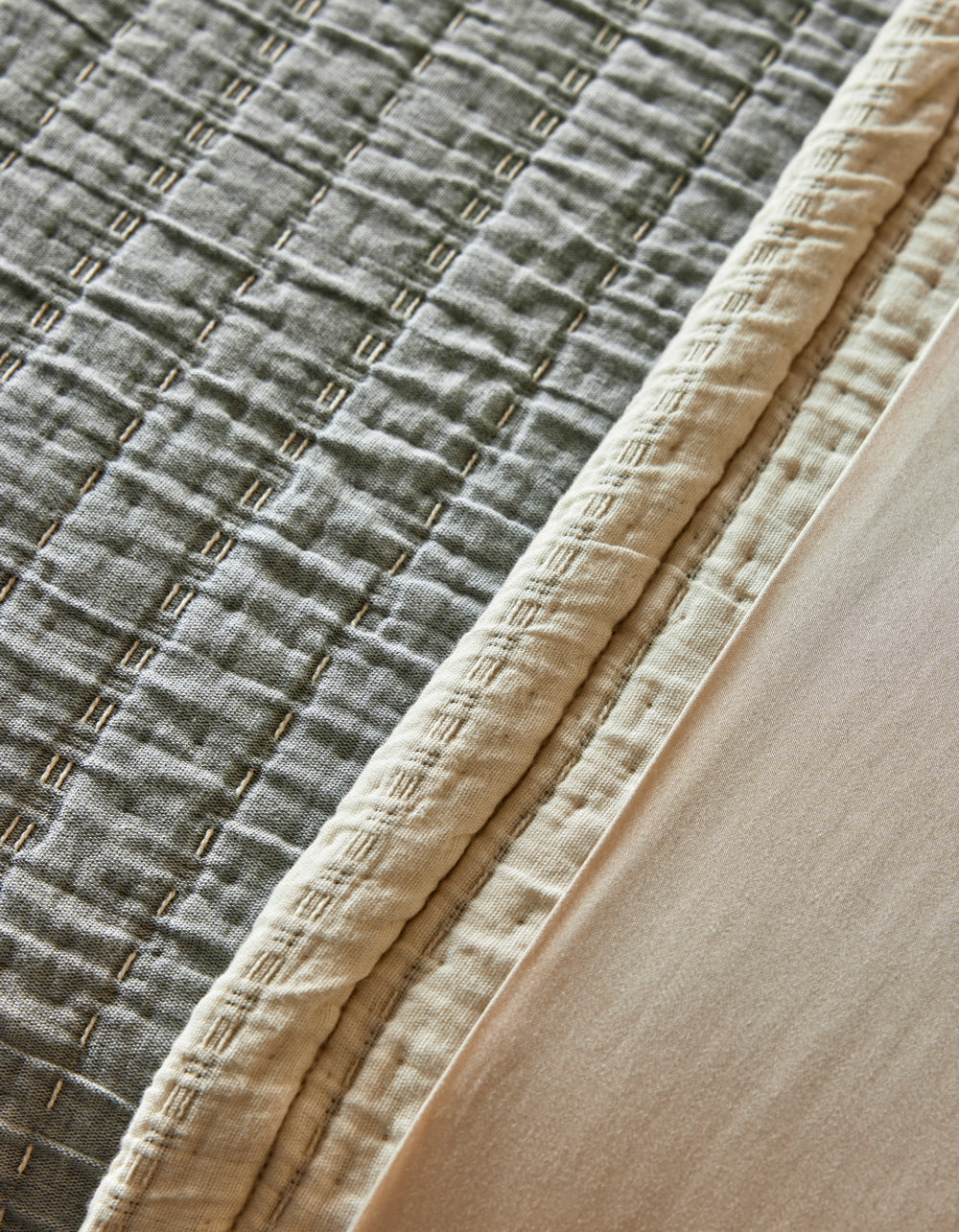 Close-up of the Cozy Earth Baja Matelasse Coverlet, featuring a stitched geometric texture, cream border, and smooth light beige fabric alongside.