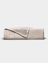 The Cozy Earth Baja Matelasse Coverlet, folded to display its textured beige and light brown fabric with one corner turned down, is pictured against a plain white background.|Color:Ebony/Taupe