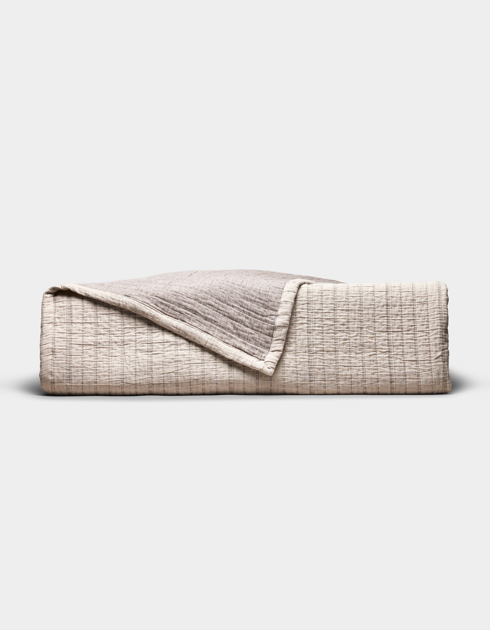 The Cozy Earth Baja Matelasse Coverlet, folded to display its textured beige and light brown fabric with one corner turned down, is pictured against a plain white background.