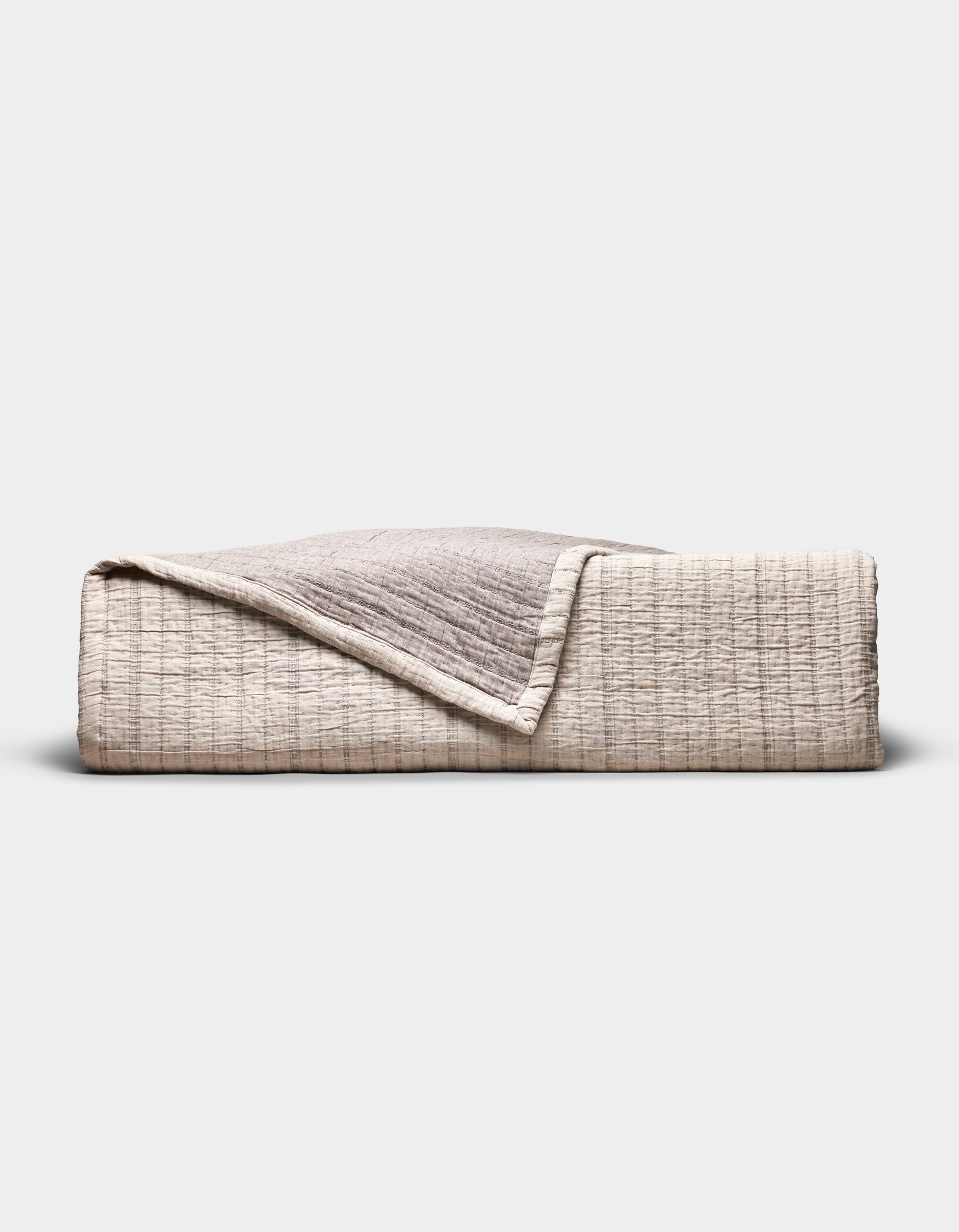 The Cozy Earth Baja Matelasse Coverlet, folded to display its textured beige and light brown fabric with one corner turned down, is pictured against a plain white background.|Color:Ebony/Taupe
