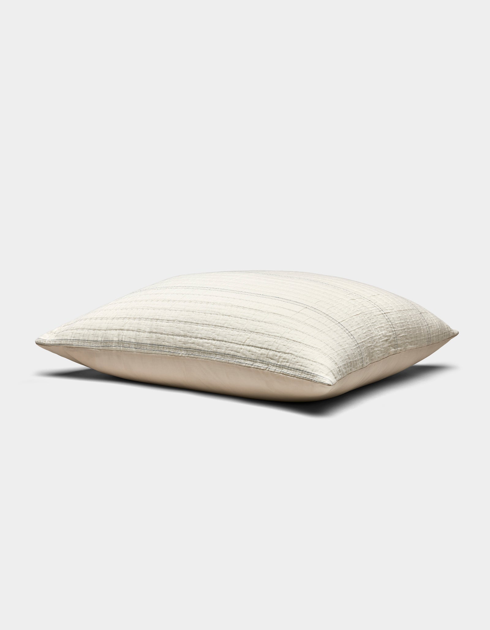 The Baja Matelasse Sham by Cozy Earth is a rectangular, light beige pillow with a subtle striped texture, pictured resting on a flat surface against a plain white background.