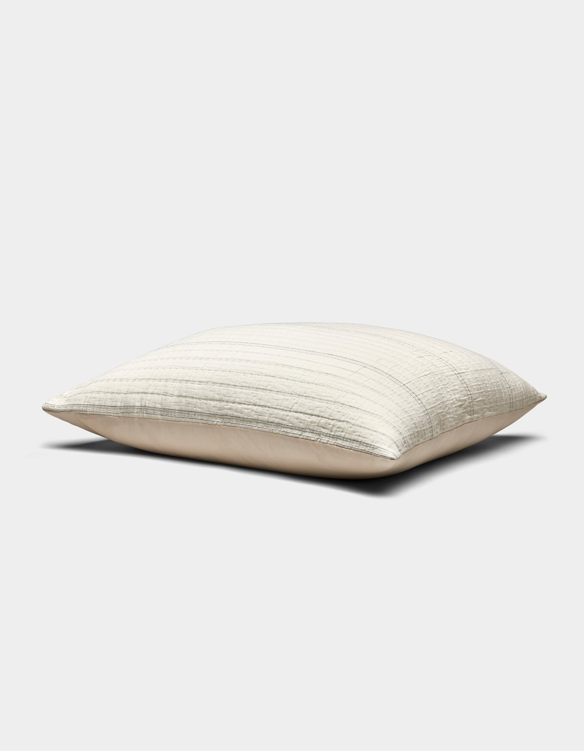 The Baja Matelasse Sham by Cozy Earth is a rectangular, light beige pillow with a subtle striped texture, pictured resting on a flat surface against a plain white background.