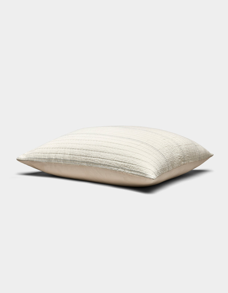 The Baja Matelasse Sham by Cozy Earth is a rectangular, light beige pillow with a subtle striped texture, pictured resting on a flat surface against a plain white background.