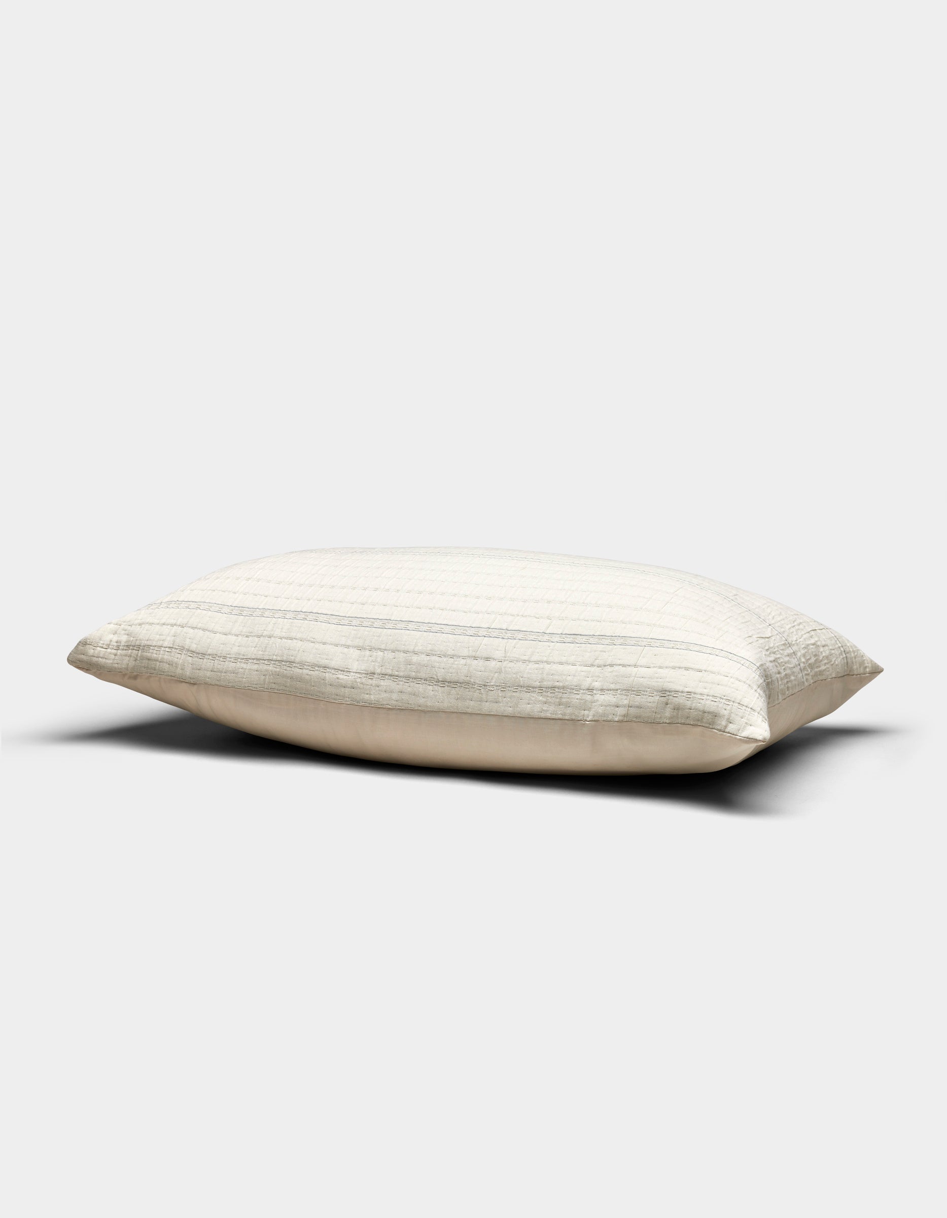 The Baja Matelasse Sham by Cozy Earth, in a cream shade with subtle horizontal stripes, rests on a plain light gray background. Its soft, gently flattened appearance suggests both comfort and support.|Color:Alabaster/Oceanside