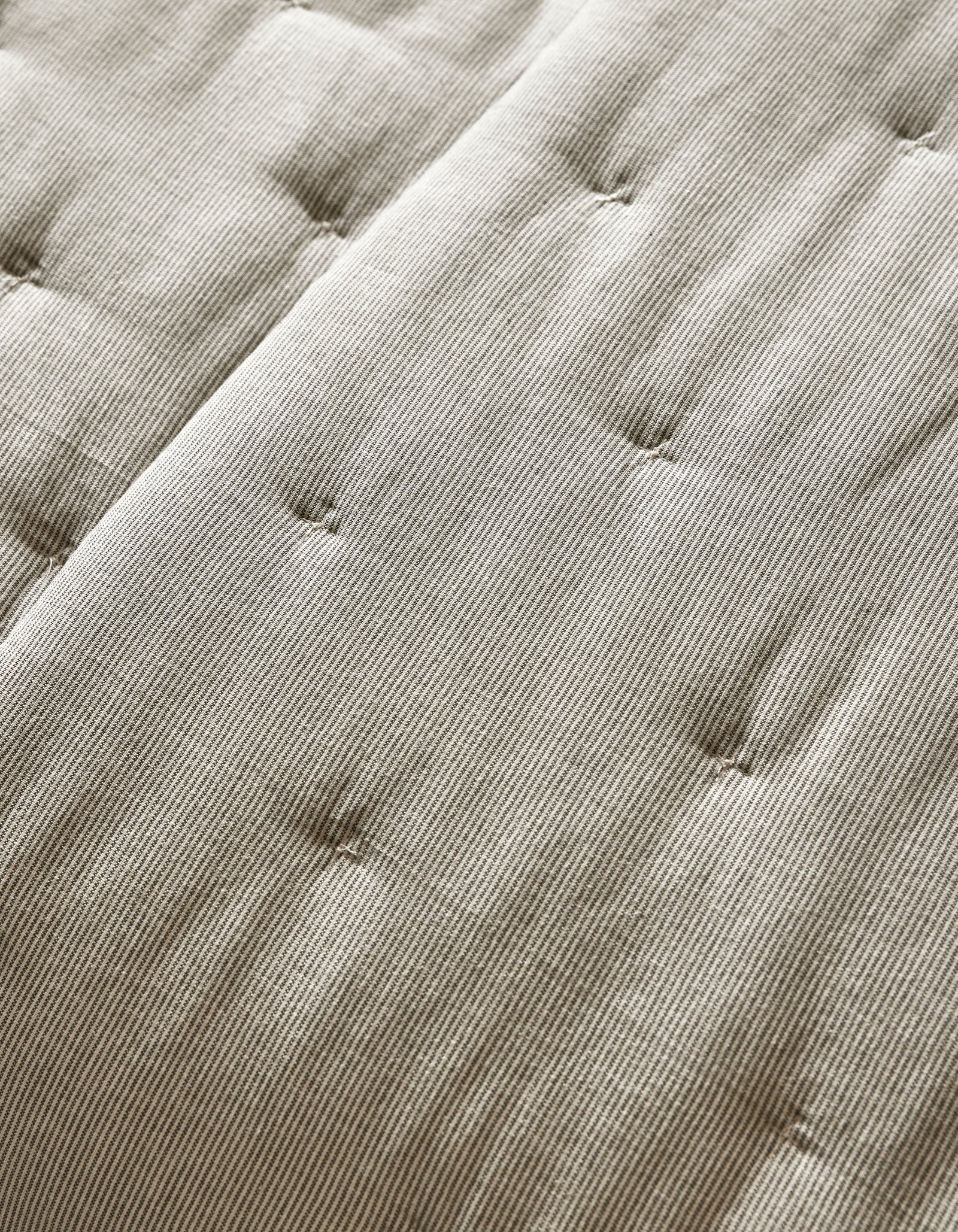 Close-up of the Cozy Earth Baja Quilt’s beige, textured surface featuring parallel lines and button-like tufts for a quilted, cushioned look.