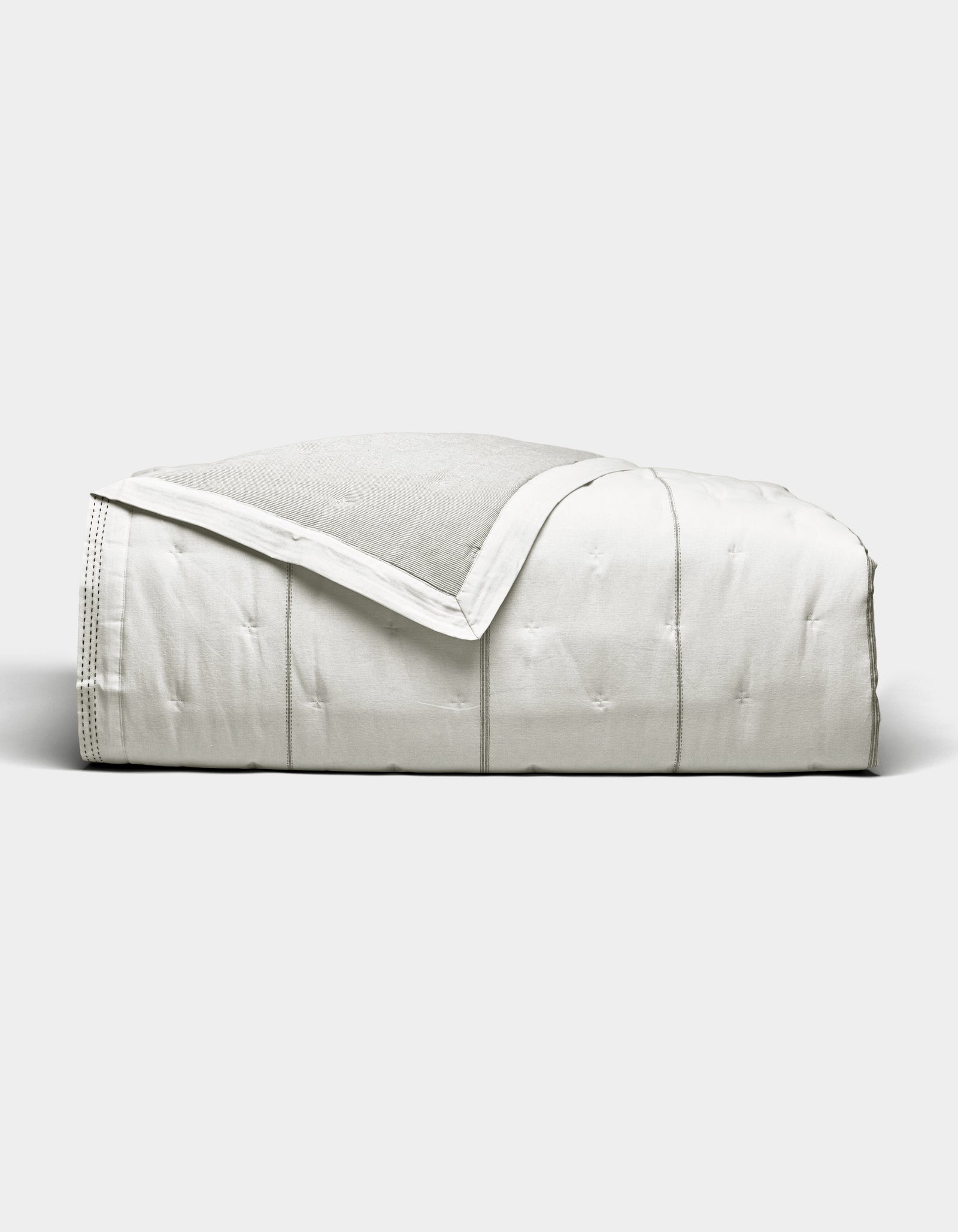 The Cozy Earth Baja Quilt, featuring stitched detailing, is neatly folded and displayed against a plain light gray background.