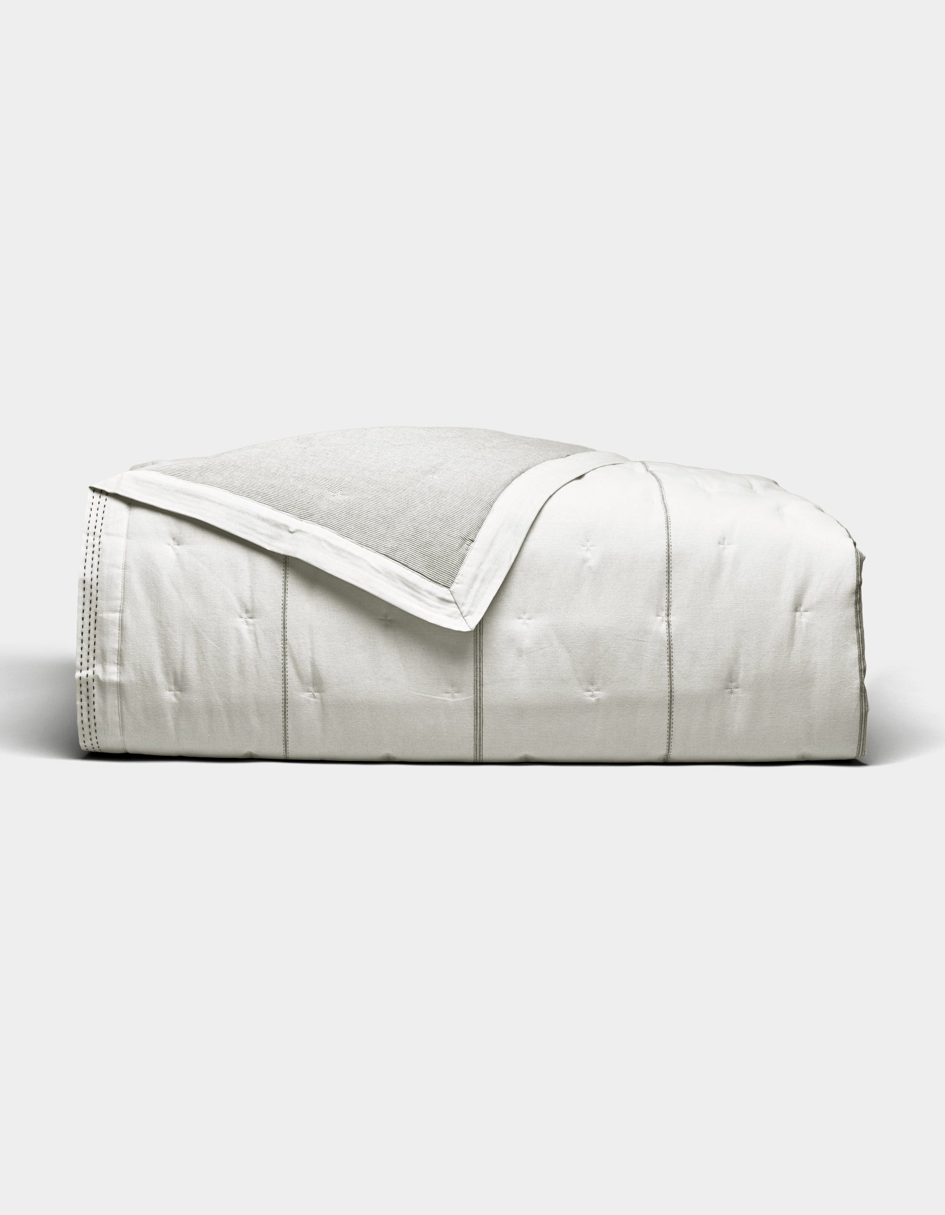 The Cozy Earth Baja Quilt, featuring stitched detailing, is neatly folded and displayed against a plain light gray background.