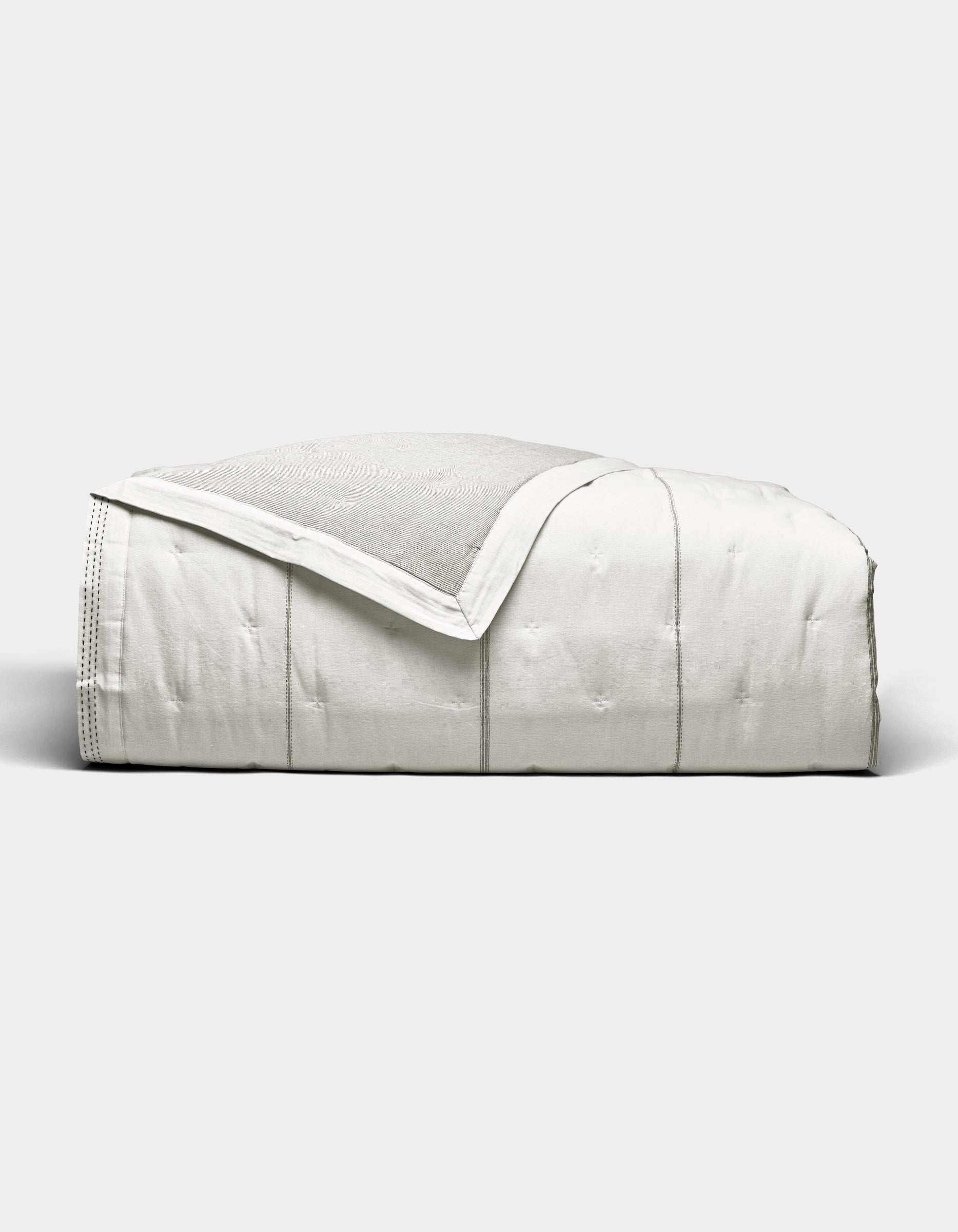 The Baja Quilt by Cozy Earth, a neatly folded white quilted blanket with a soft, smooth texture, is displayed against a plain light gray background.