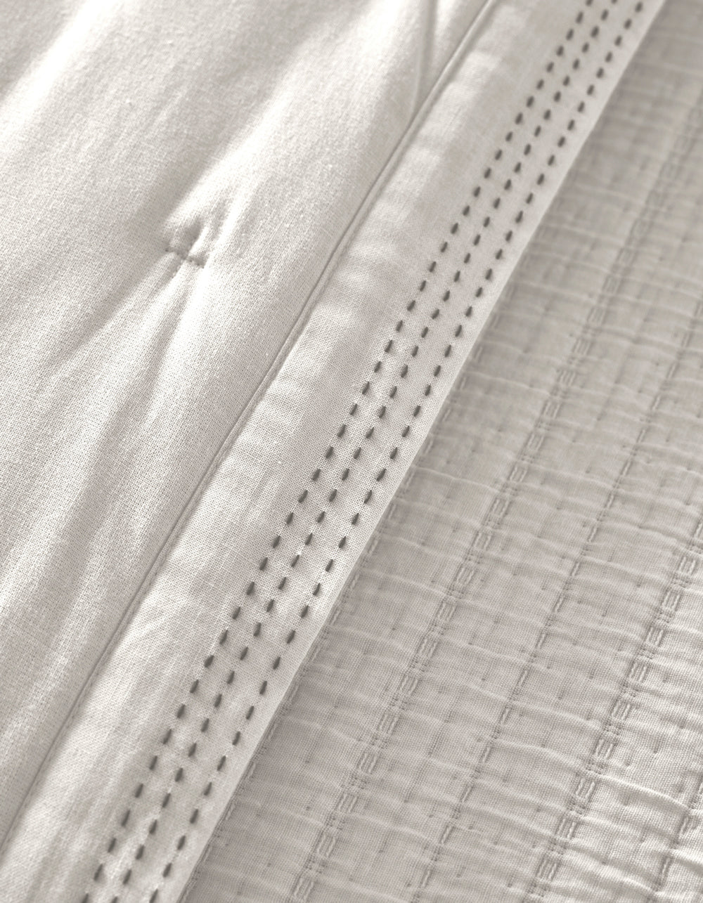 Close-up of the Cozy Earth Baja Quilt in white, featuring quilted stitching and a decorative perforated hem that highlights the soft, textured woven details.