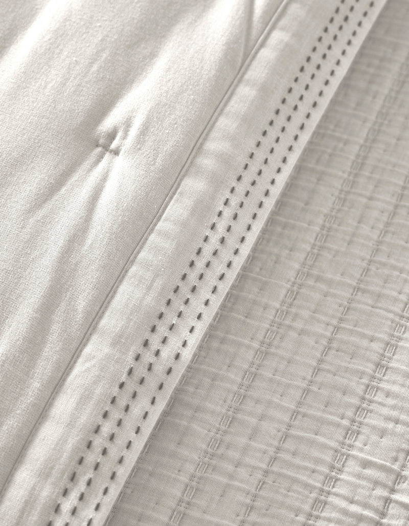 Close-up of the Cozy Earth Baja Quilt in white, featuring quilted stitching and a decorative perforated hem that highlights the soft, textured woven details.