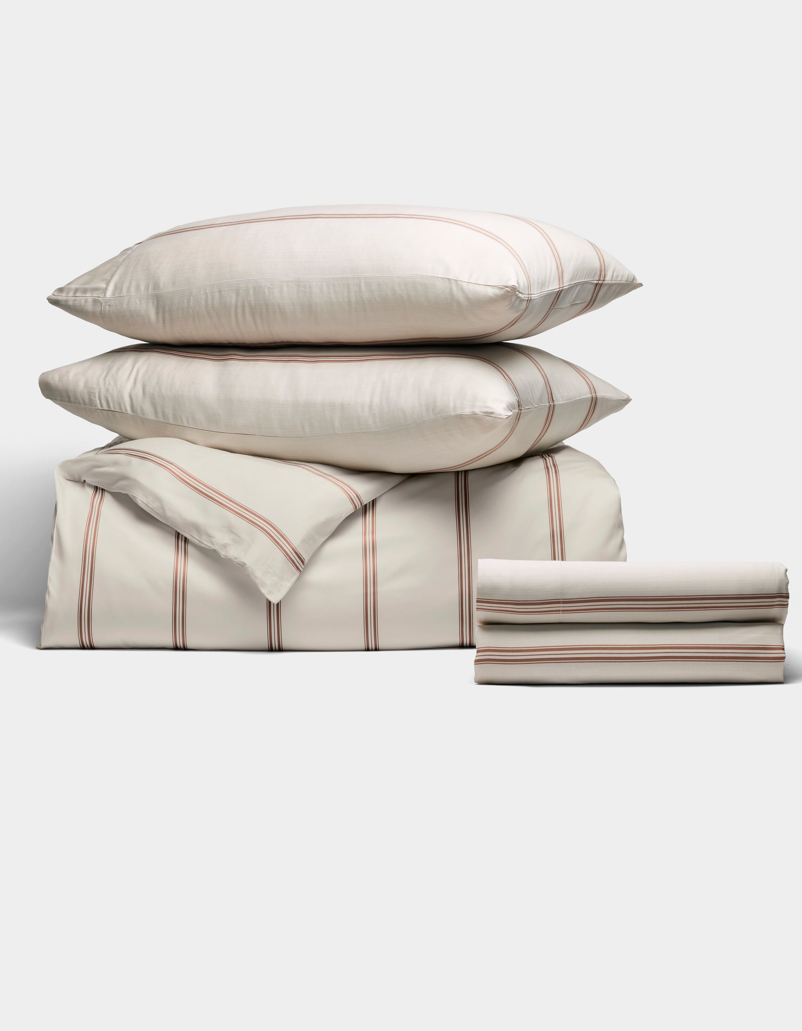 The Cozy Earth Bamboo Bedding Deluxe Bundle features a neatly stacked set with thin red and gray stripes on a cream background, including two large pillows, a folded comforter, and two sheets, displayed against a light backdrop.