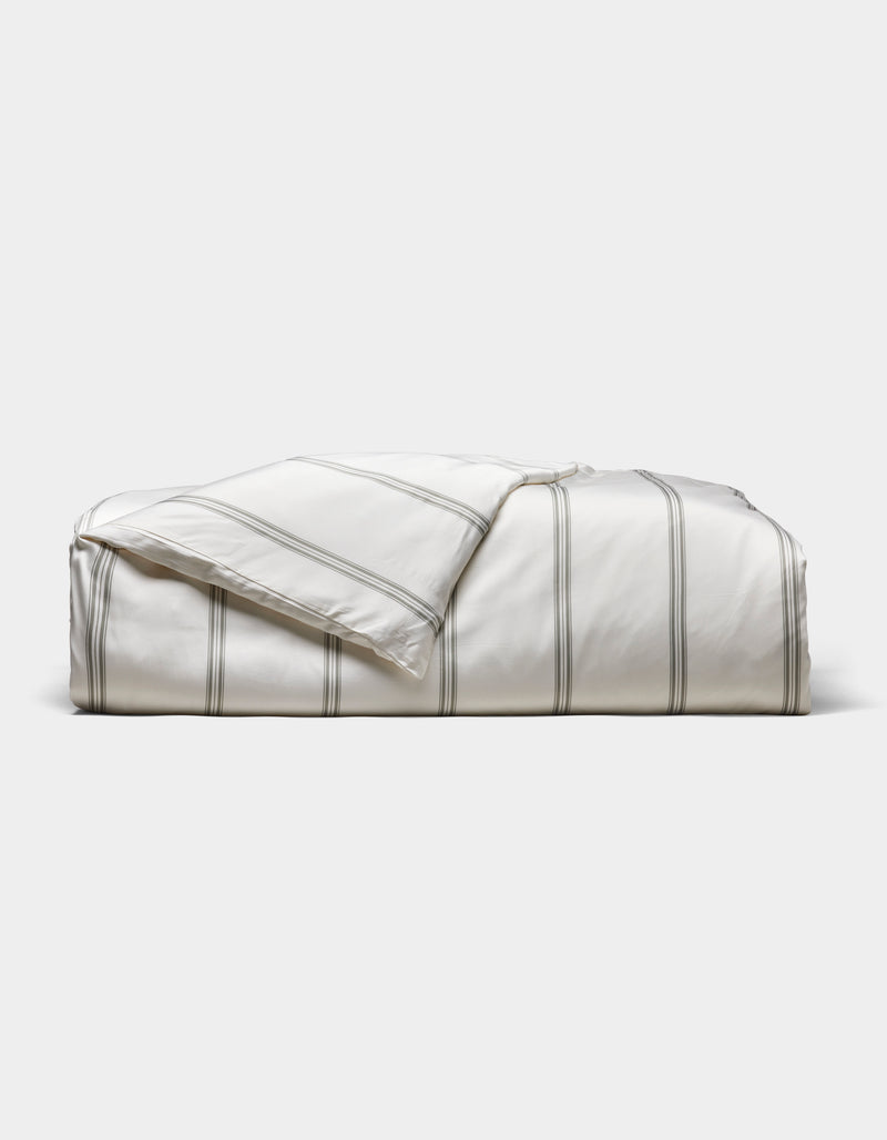 The Cozy Earth Bamboo Duvet Cover, white with thin gray stripes, is neatly folded against a light gray background. A corner is turned down to reveal the underside.