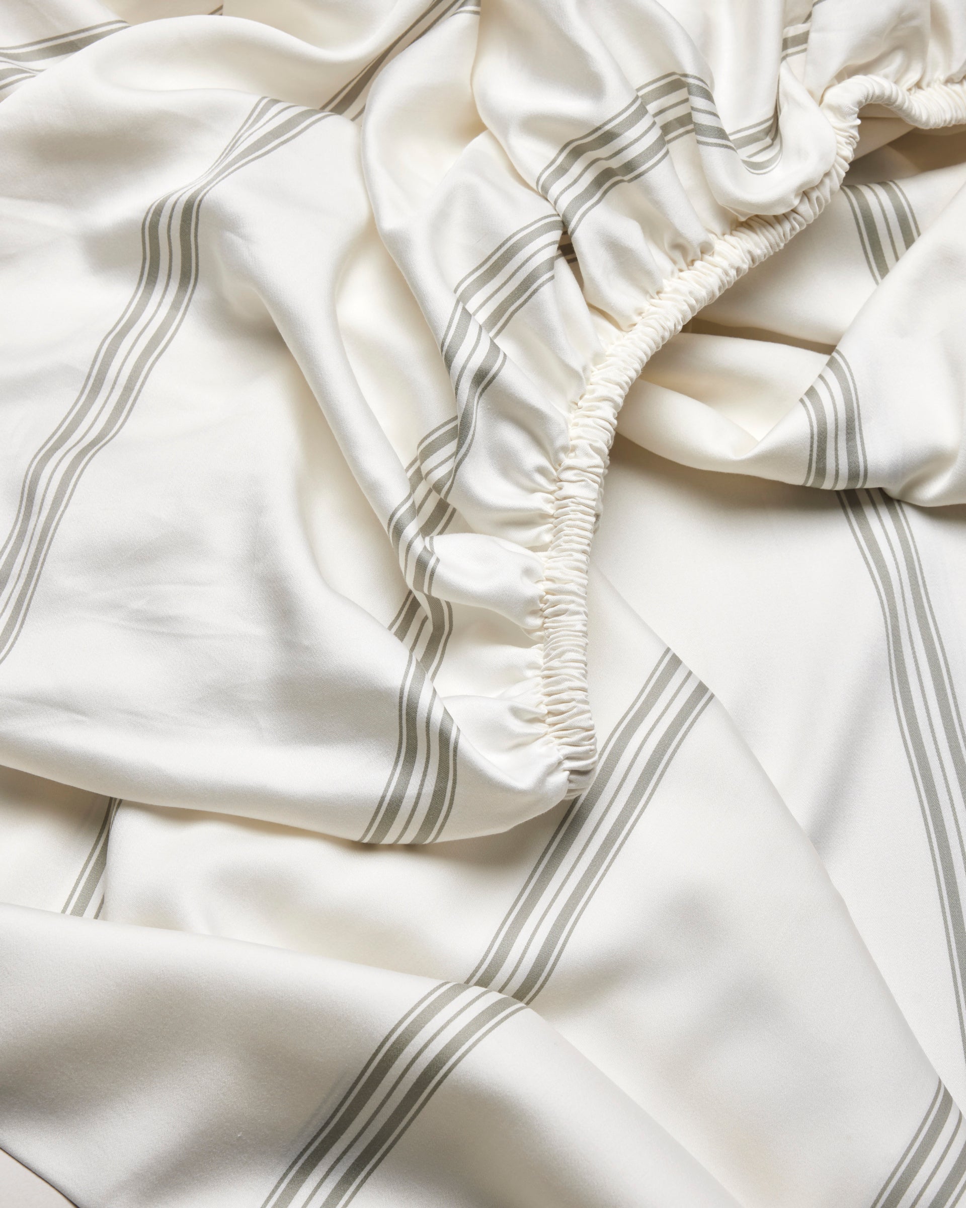 A close-up of the Cozy Earth Bamboo Fitted Sheet, featuring soft, smooth fabric with light gray stripes and gathered elastic edges.|Color:Baja Stripe in Laurel