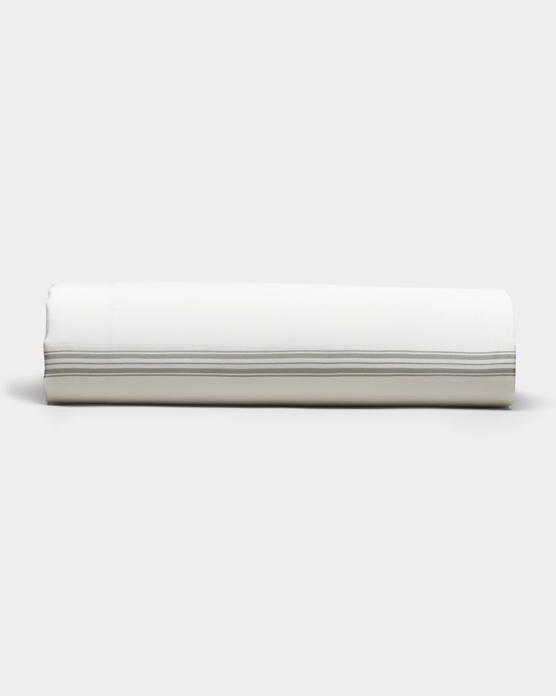 The Bamboo Sheet Set by Cozy Earth is shown neatly rolled, featuring subtle horizontal gray stripes near the edge, set against a plain light gray background.