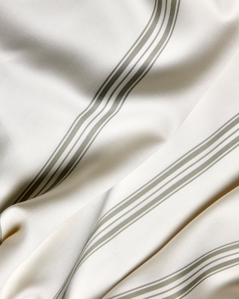 A close-up of Cozy Earth’s Bamboo Sheet Set shows ivory fabric with parallel gray stripes, soft folds, and a smooth texture.