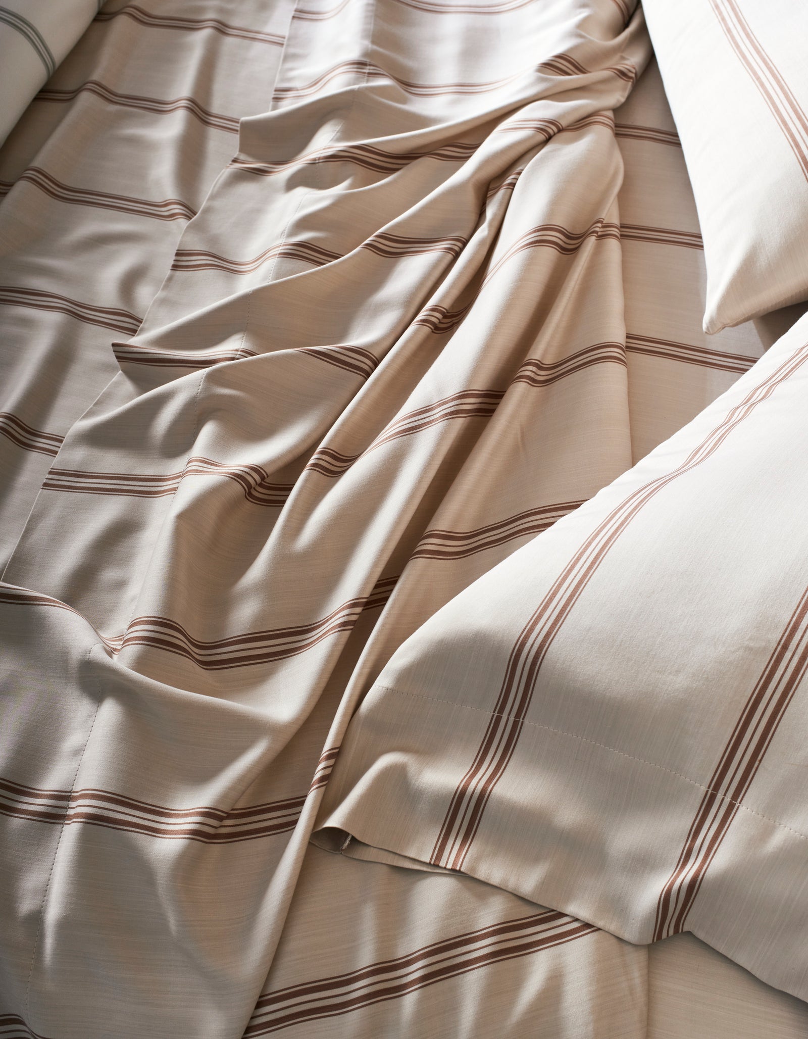 A close-up of the Cozy Earth Bamboo Sheet Set shows cream-colored sheets with brown horizontal stripes, slightly rumpled, and two pillows placed on either side.