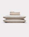 Two cream-colored pillows are stacked with Cozy Earth’s Bamboo Sheet Set, neatly folded on top, all arranged against a plain white background.|Color:Baja Stripe in Maple