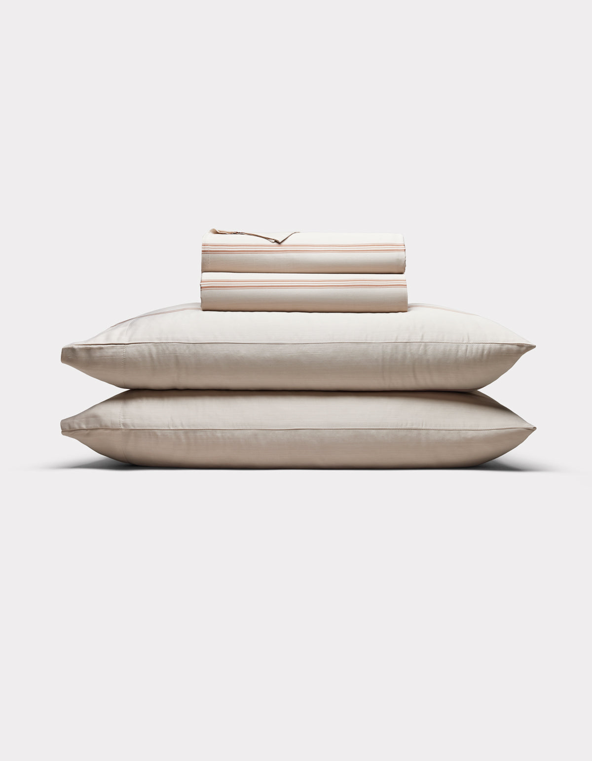 Two cream-colored pillows are stacked with Cozy Earth’s Bamboo Sheet Set, neatly folded on top, all arranged against a plain white background.