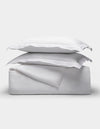 The Linen Duvet Set by Cozy Earth is shown neatly folded with two stacked pillows, arranged on top of folded sheets against a plain light background.|Color:White