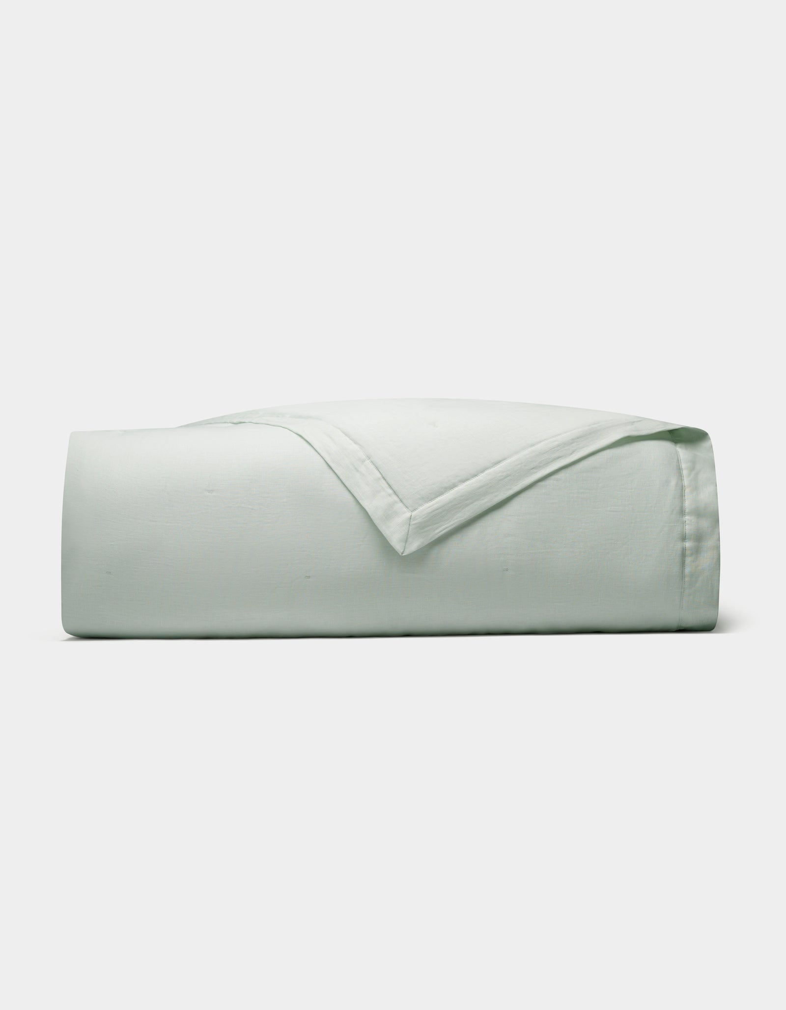 The Cozy Earth Linen Quilt, in a light green shade, is neatly folded and displayed against a plain white background.