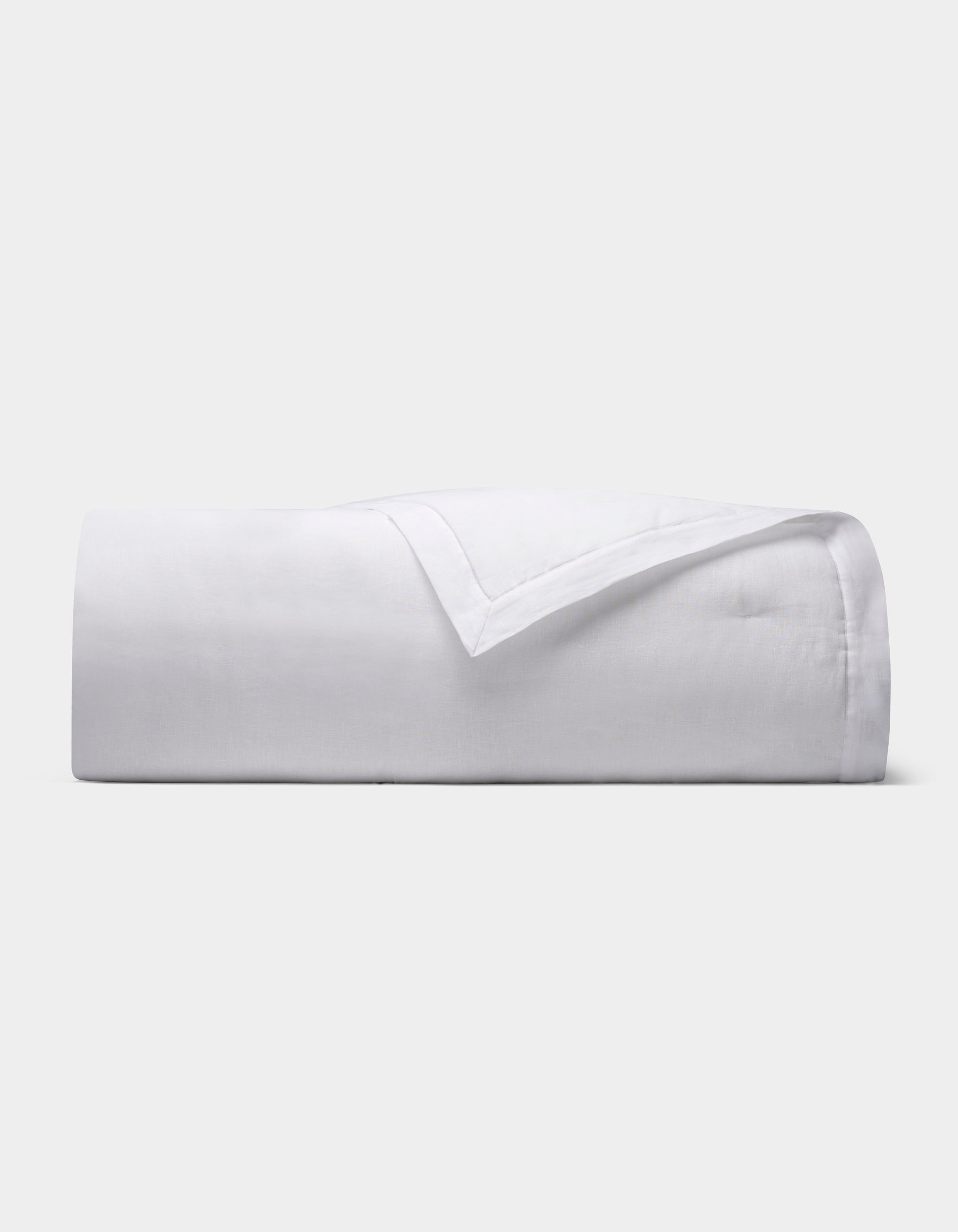 The Cozy Earth Linen Quilt, featuring a smooth texture, is neatly folded and displayed against a plain light gray background.|Color:White