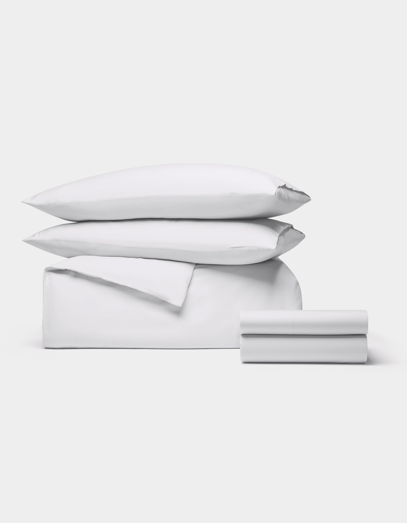 The Cozy Earth Soft-Wash Cotton Bedding Deluxe Bundle, featuring two pillows, a duvet cover, and two sheets in white, is neatly stacked against a plain light gray background.