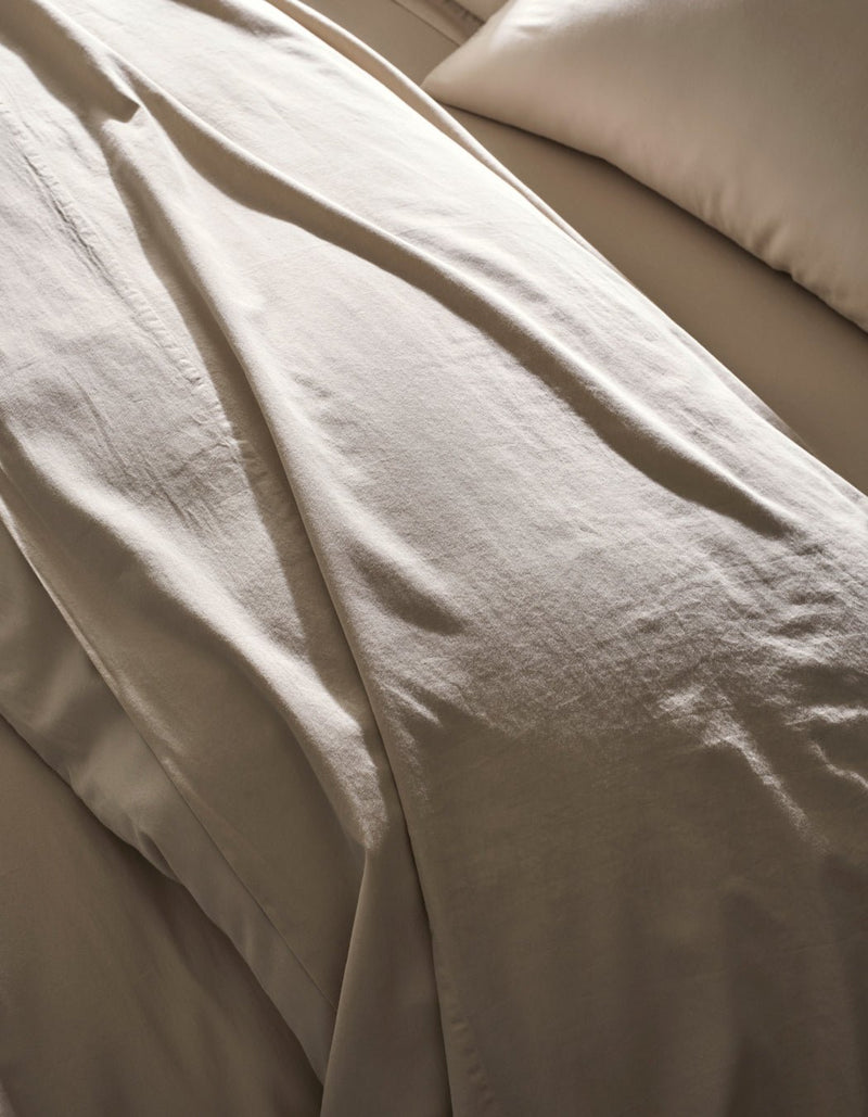 Close-up of a neatly made bed with Cozy Earth's Soft-Wash Cotton Duvet Cover in beige, featuring a matching pillow. The soft, smooth fabric is highlighted by gentle natural light, showcasing its luxurious texture.