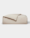 The Cozy Earth Soft-Wash Cotton Duvet Cover, in light beige, is neatly folded with one corner partially flipped over and displayed against a plain white background.|Color:Driftwood