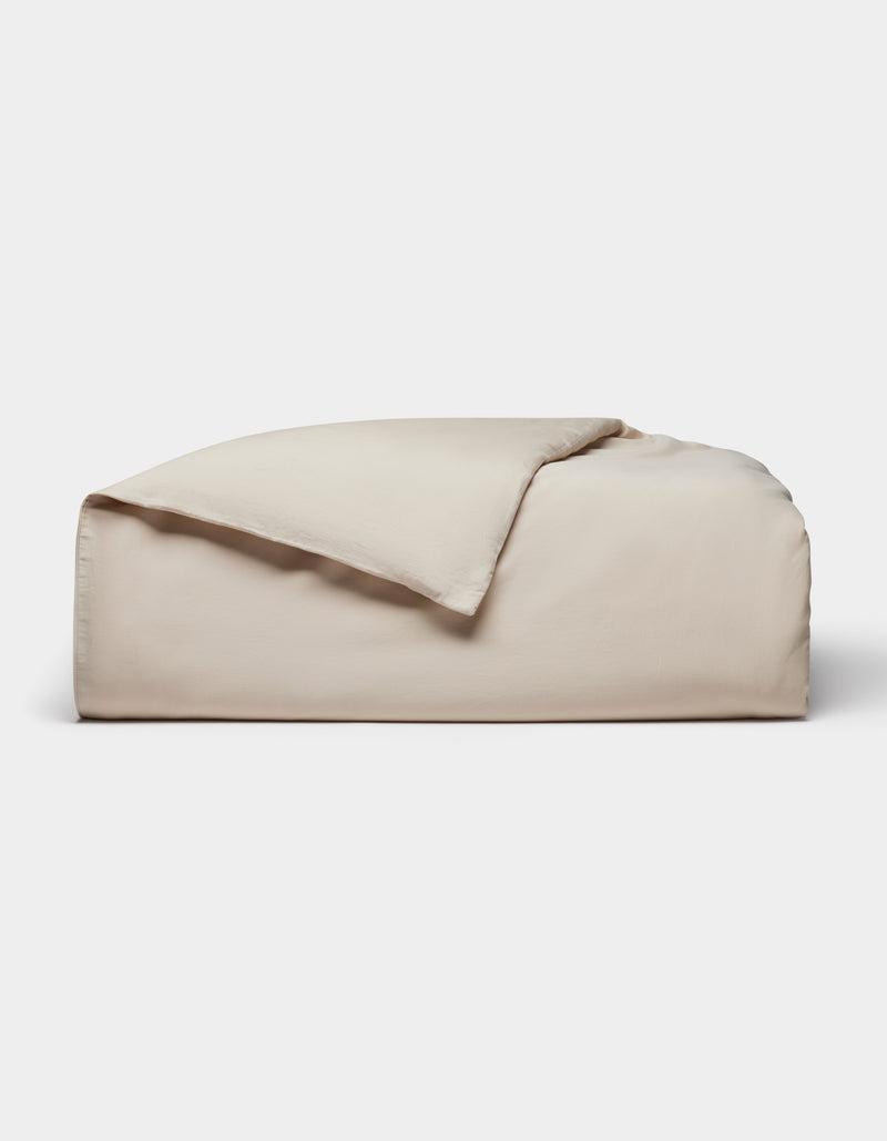 The Cozy Earth Soft-Wash Cotton Duvet Cover, in light beige, is neatly folded with one corner partially flipped over and displayed against a plain white background.