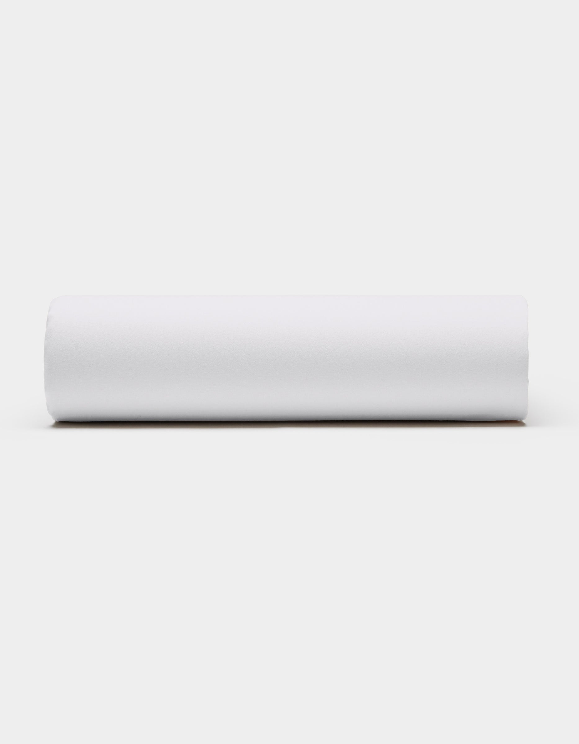 A Soft-Wash Cotton Fitted Sheet by Cozy Earth, in plain white, is displayed horizontally against a light gray background, viewed from the side.