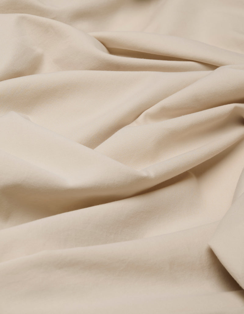 The Cozy Earth Soft-Wash Cotton Flat Sheet features cream-colored fabric with a soft texture, showcased in gentle folds and wrinkles for a smooth, cozy look.